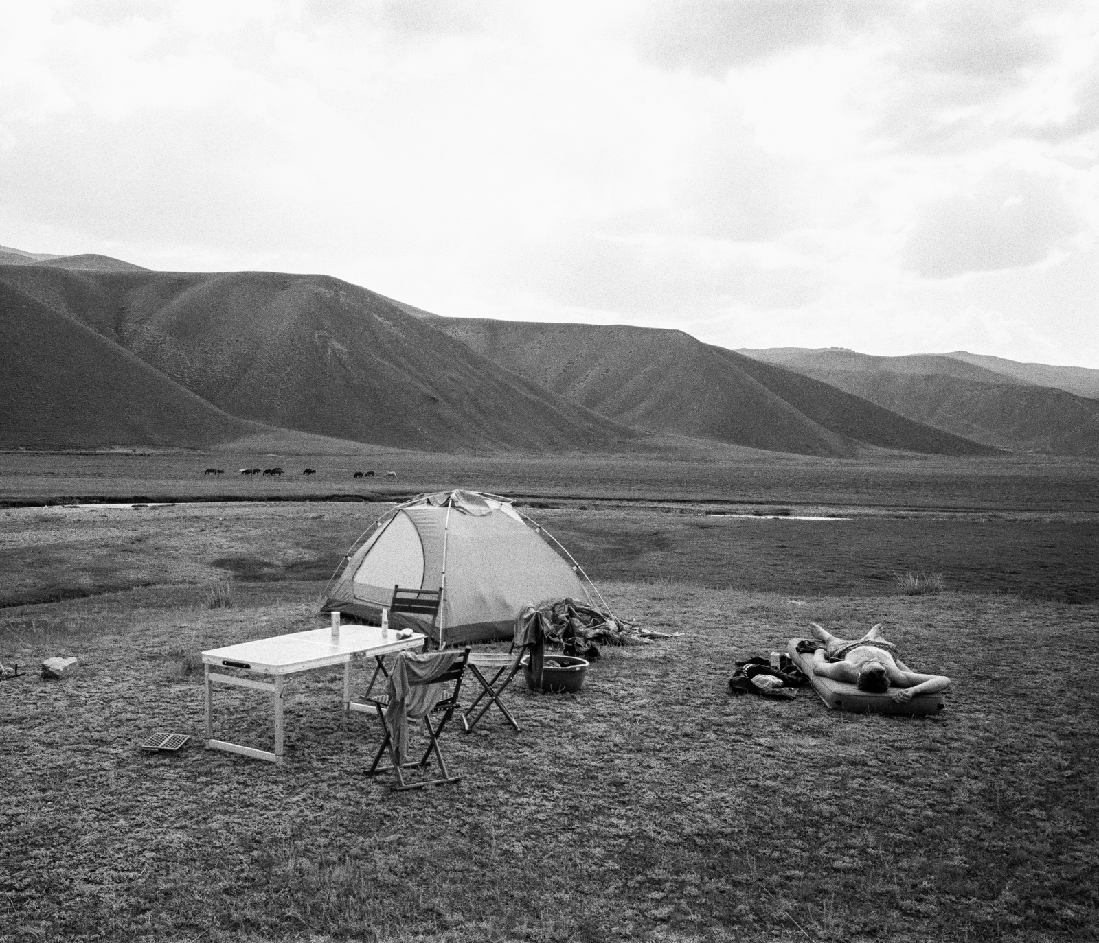 black and white camp set beneath rounded mountain ridges